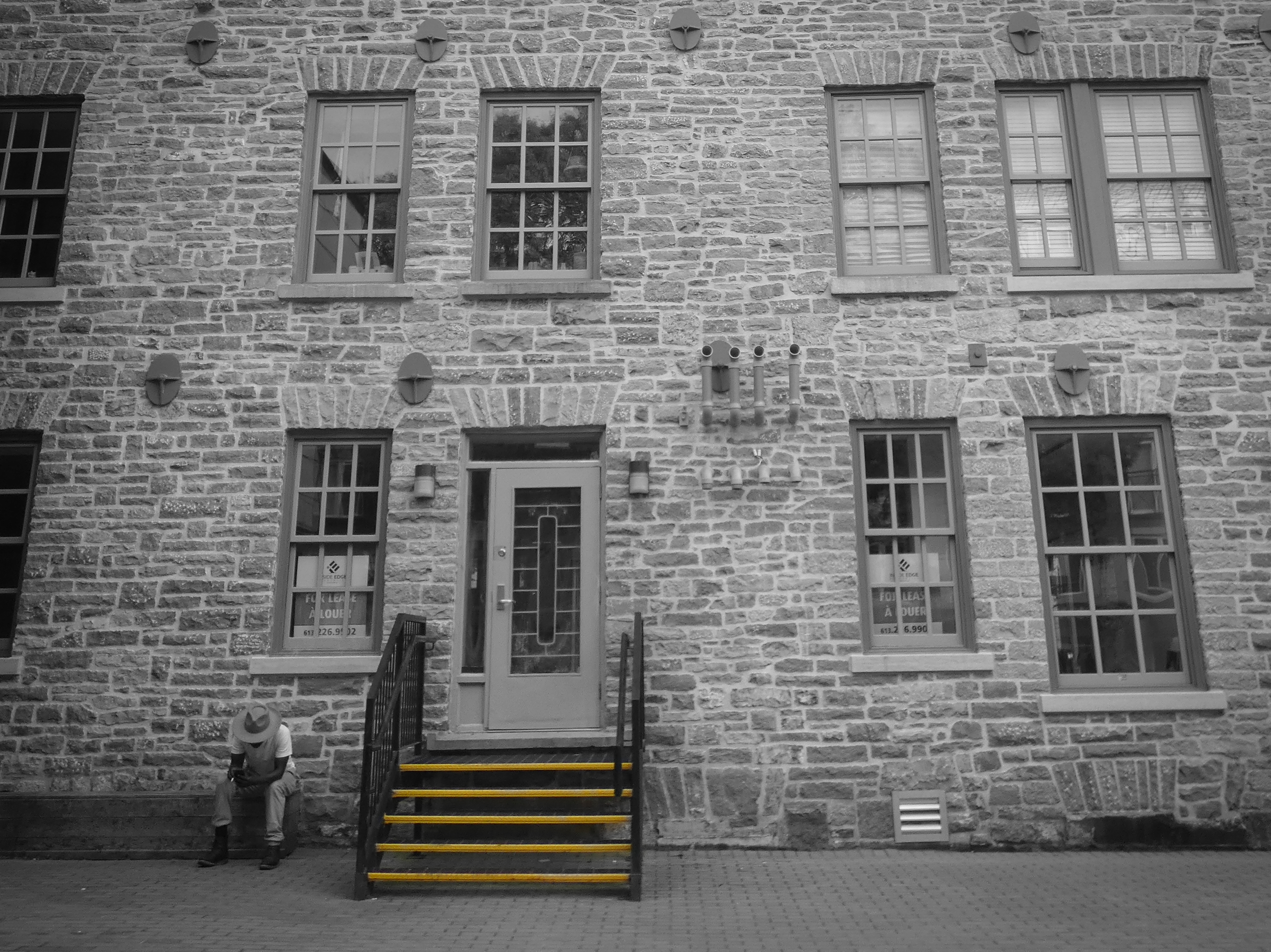 a lone man sits outside a heritage building looking at his phone next to the steps
