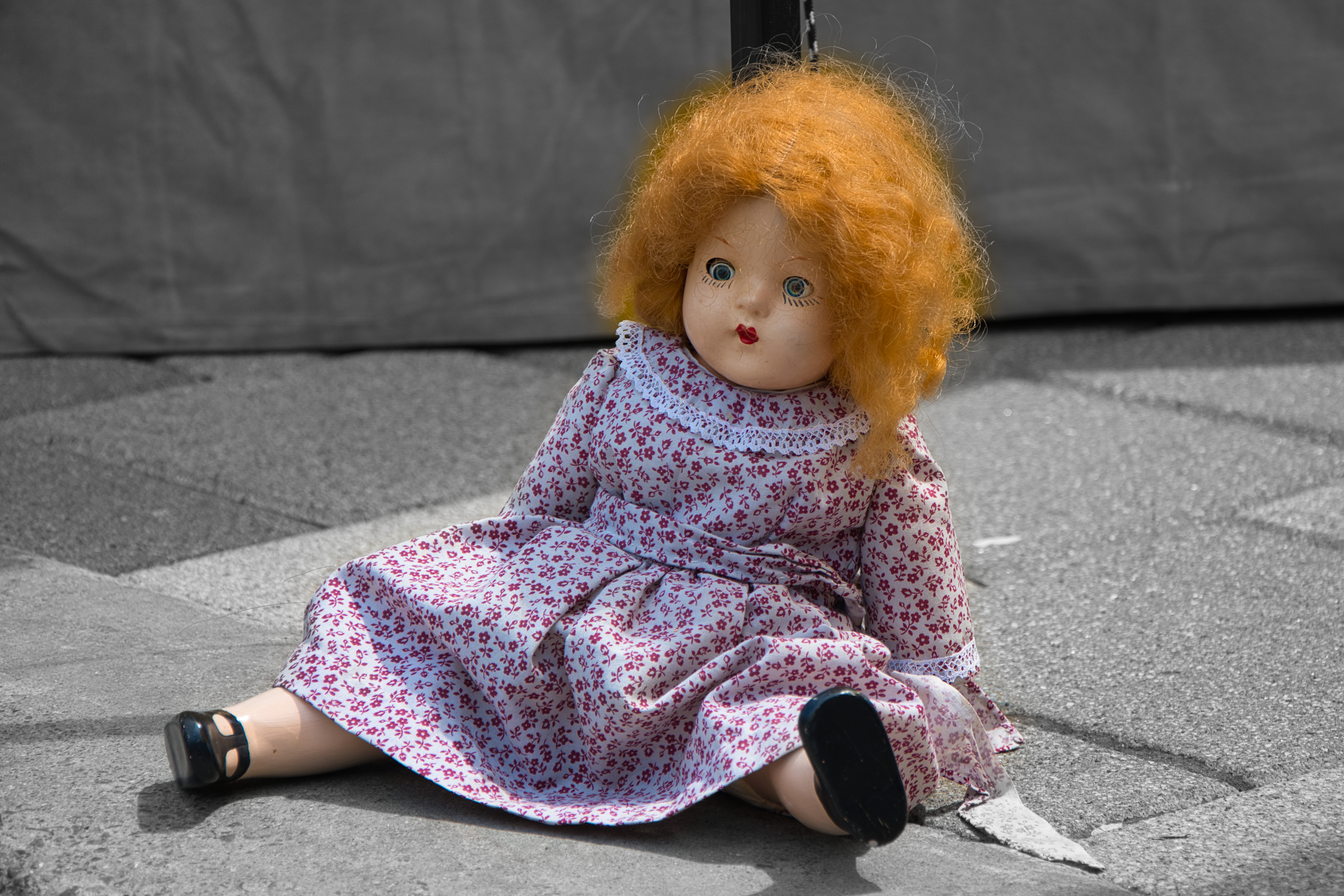 an old fashioned doll with bright red hair sits on the pavement