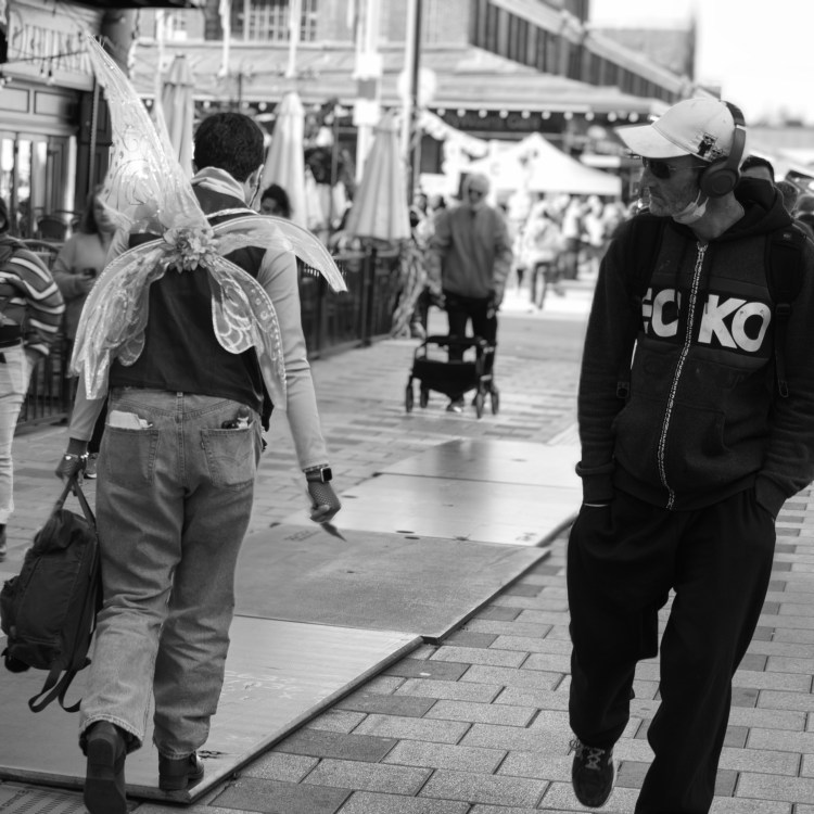 A man in the street looks at another man who has fairy wings on his back