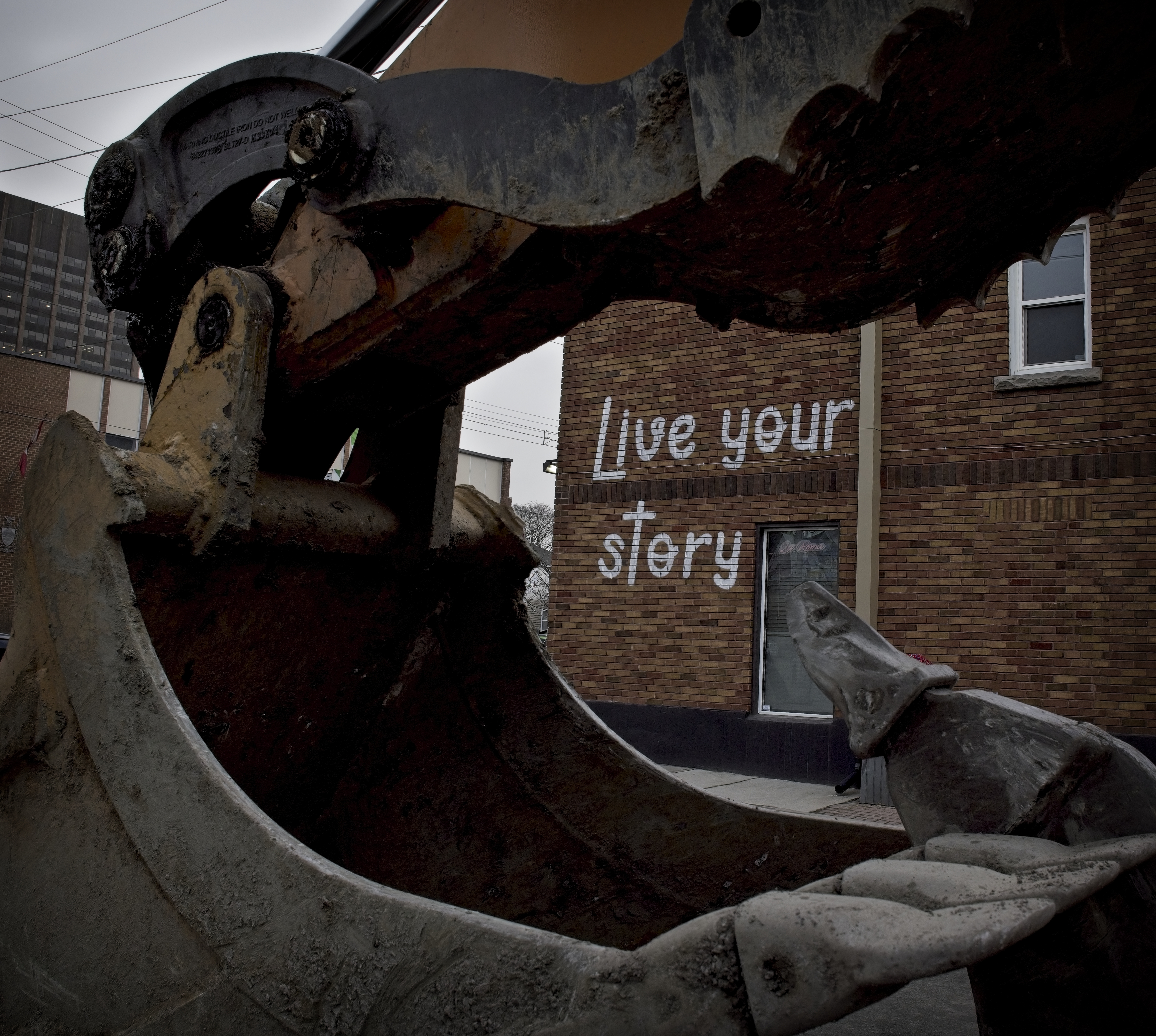 the words live your story on the side of a brick wall framed by a excavator bucket