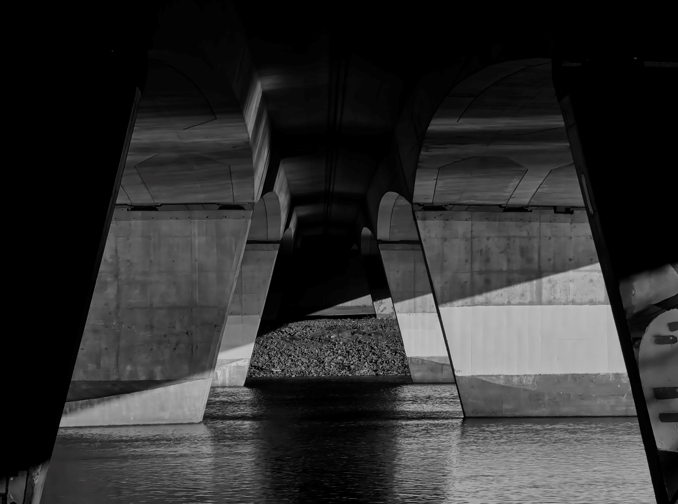 a black and white view of the concrete ramparts under a road bridge