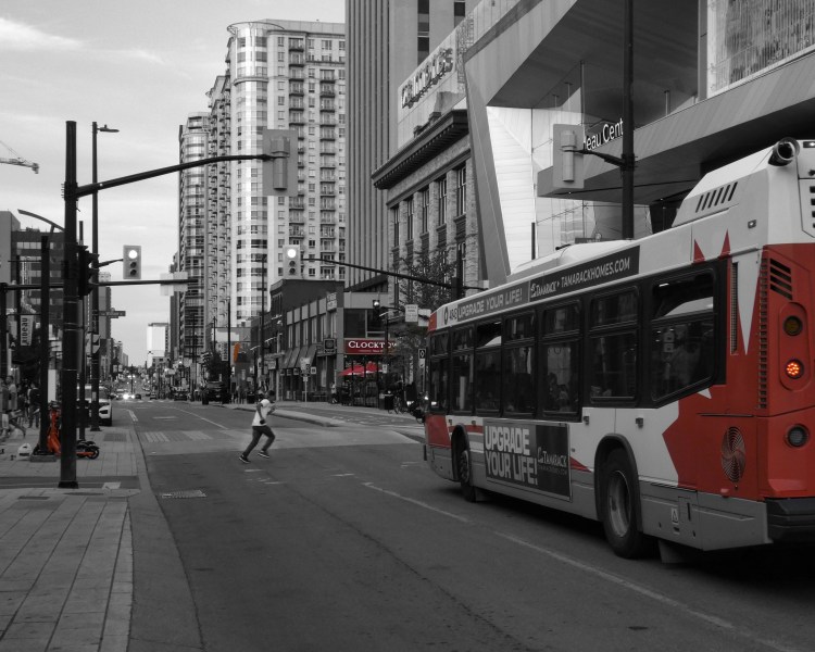 a young mans runs across a street in front of a city bus.