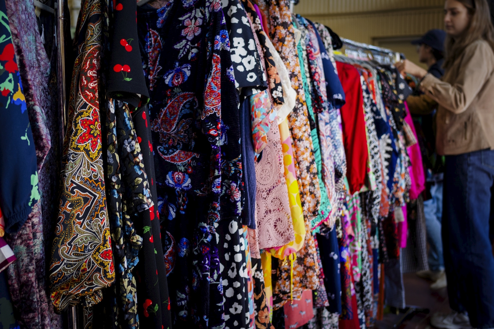a woman looks through a rack of colourful vintage dresses