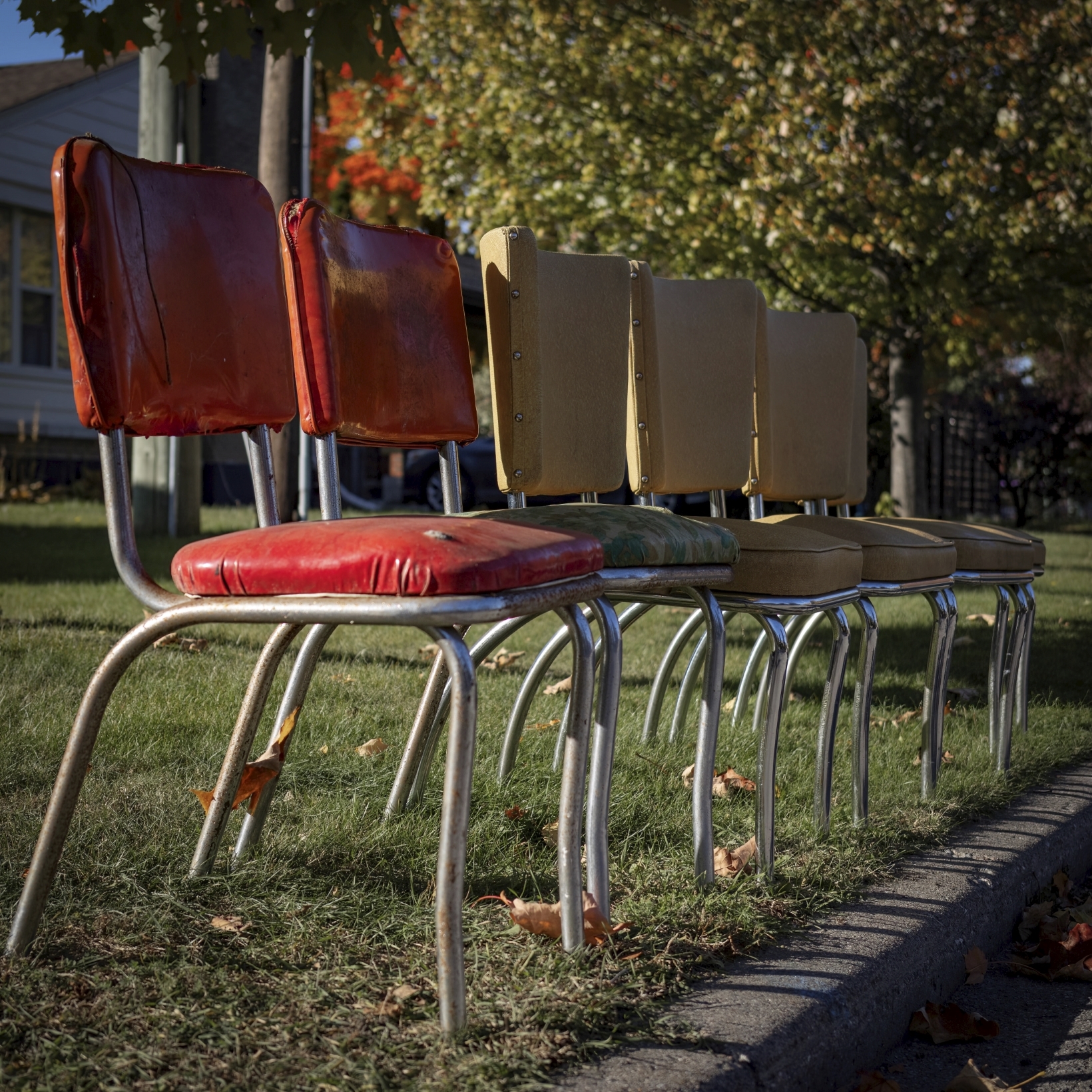six old kitchen chairs with red and yellow padded seats sit on the curb waiting for the garbage truck